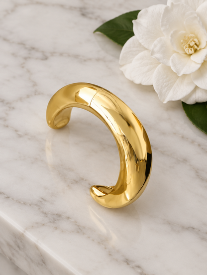 Chunky gold-tone bangle beside a white flower on marble