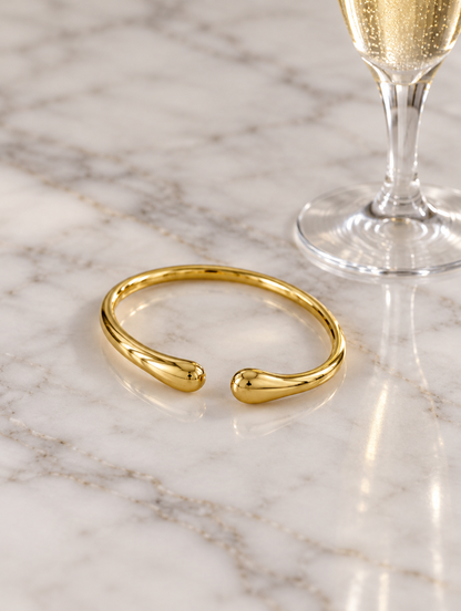Slim gold-tone teardrop cuff beside a champagne flute on marble