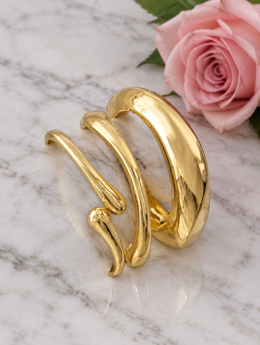 Stack of three gold-tone bangles beside a pink rose on marble