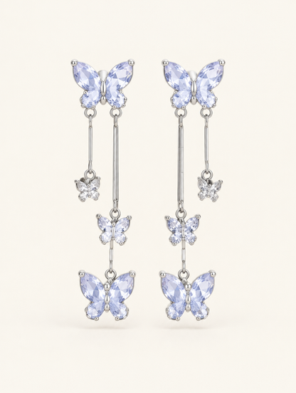 Pair of silver-lilac butterfly tassel drop earrings on a warm off-white background