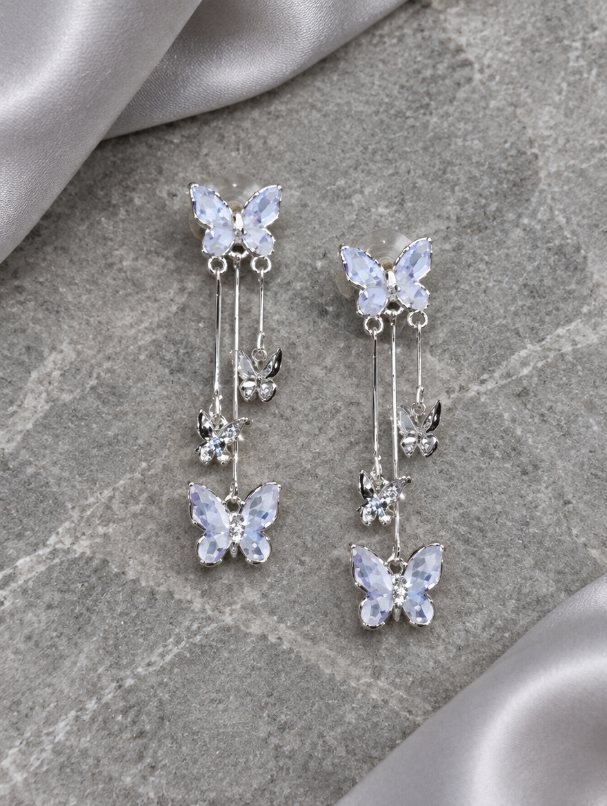 Silver-lilac butterfly tassel drop earrings lying flat on a soft styled surface