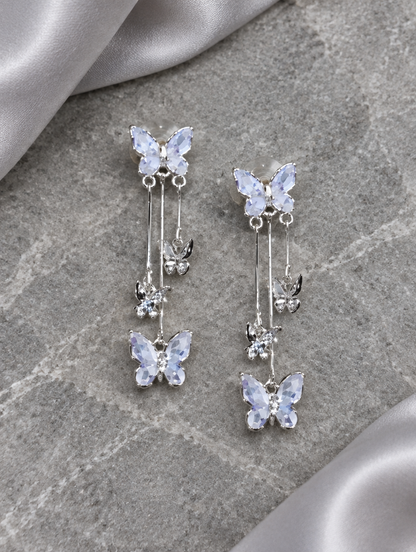 Silver-lilac butterfly tassel drop earrings lying flat on a soft styled surface