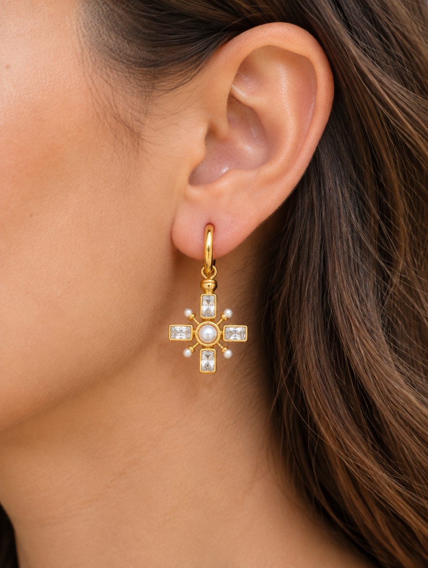 Woman wearing a gold cross drop huggie earring with pearl-look and CZ stones