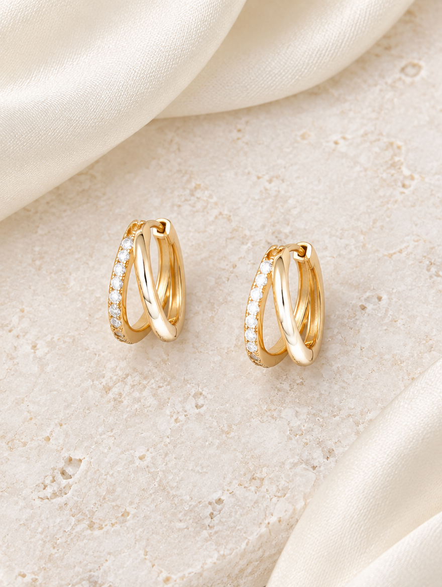 Gold double-ring CZ huggie hoop earrings lying flat on a soft styled surface