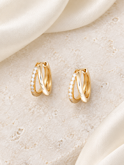 Gold double-ring CZ huggie hoop earrings lying flat on a soft styled surface