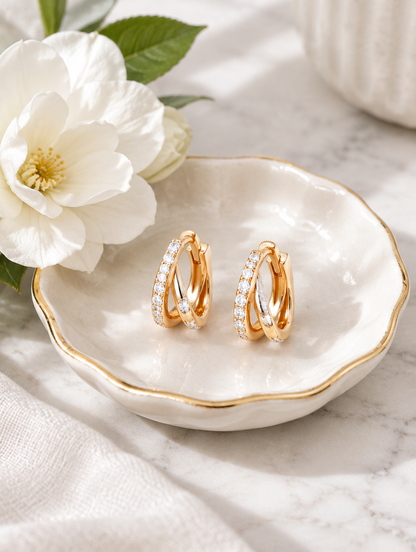 Gold double-ring CZ huggie hoop earrings in a styled still life with props
