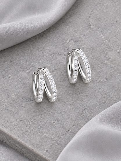 Silver double-ring CZ huggie hoop earrings lying flat on a soft styled surface