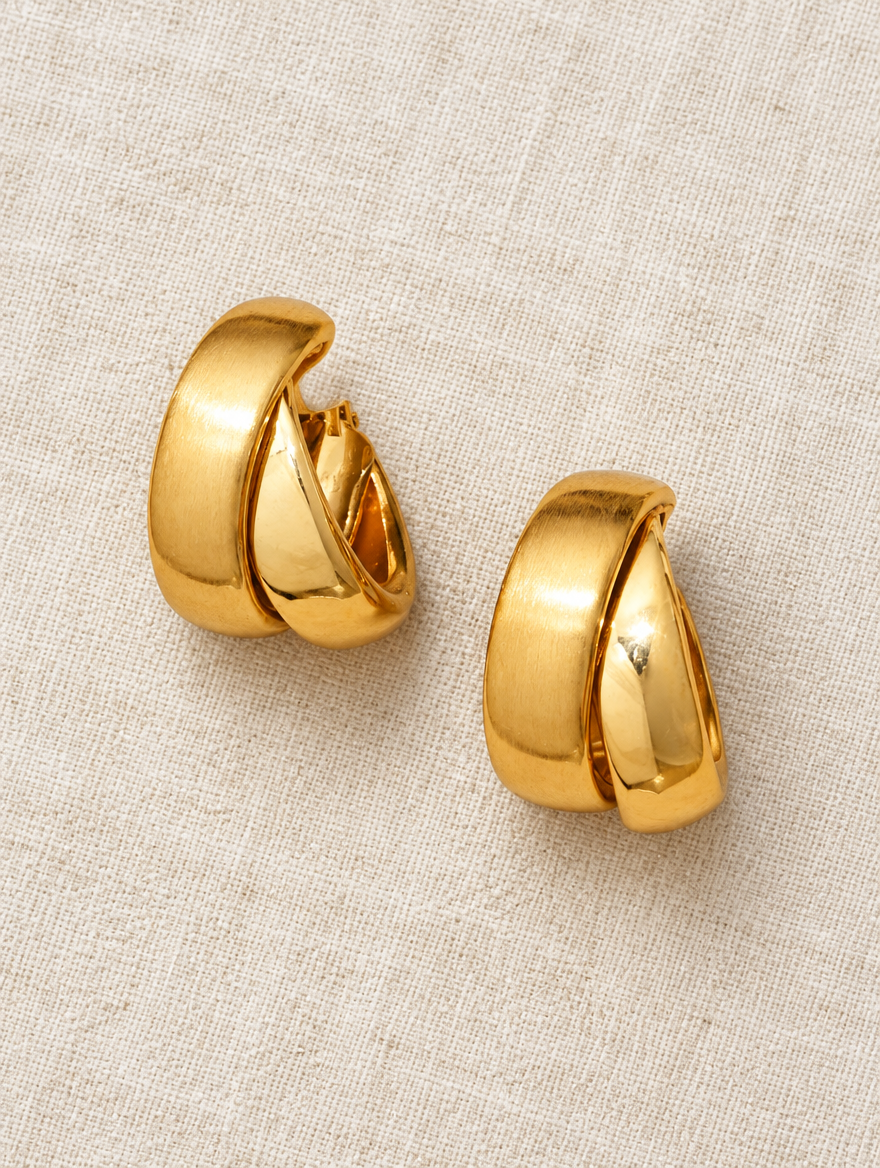 Chunky gold hoop earrings lying flat on a soft styled surface