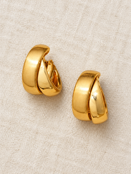 Chunky gold hoop earrings lying flat on a soft styled surface