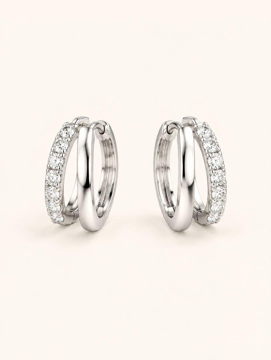 Pair of silver double-ring CZ huggie hoop earrings on a warm off-white background