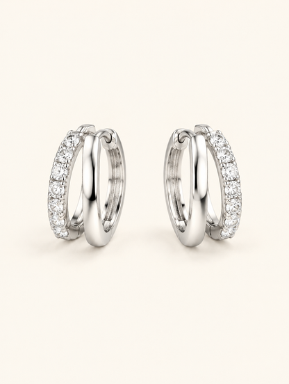 Pair of silver double-ring CZ huggie hoop earrings on a warm off-white background
