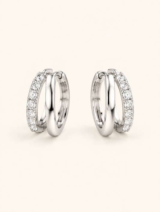Pair of silver double-ring CZ huggie hoop earrings on a warm off-white background