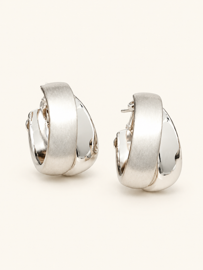 Pair of chunky silver hoop earrings on a warm off-white background
