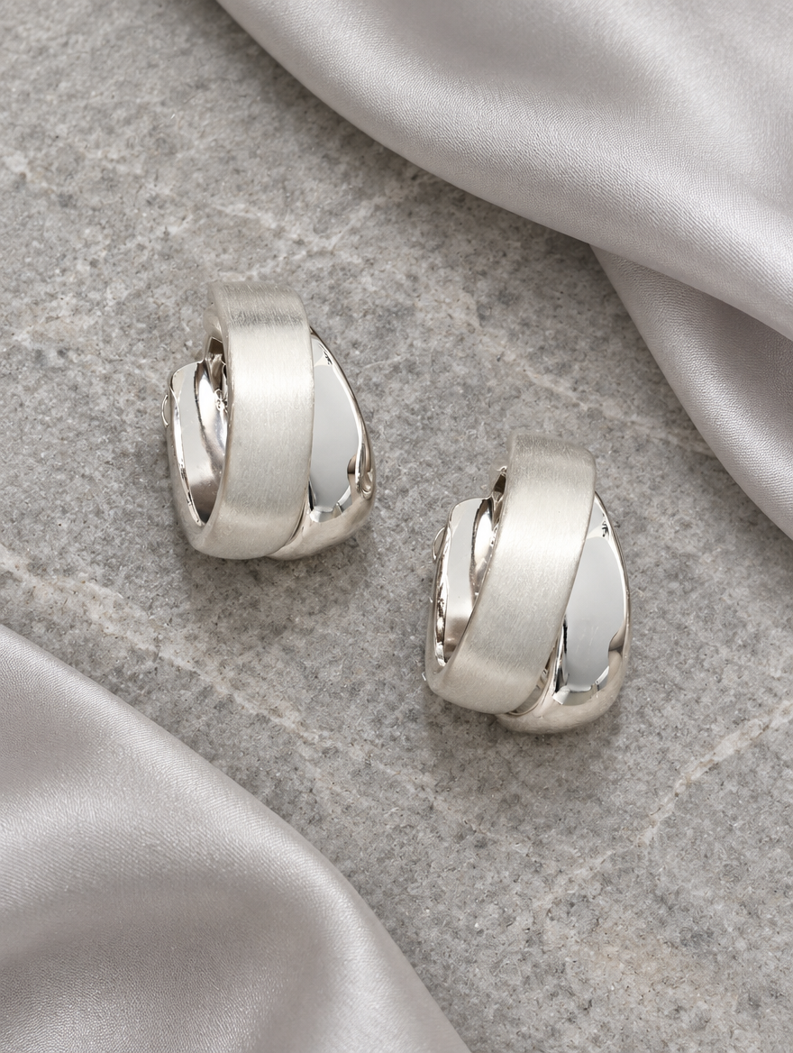 Chunky silver hoop earrings lying flat on a soft styled surface