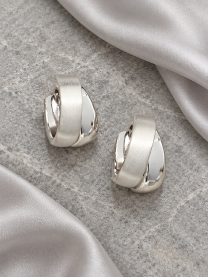 Chunky silver hoop earrings lying flat on a soft styled surface