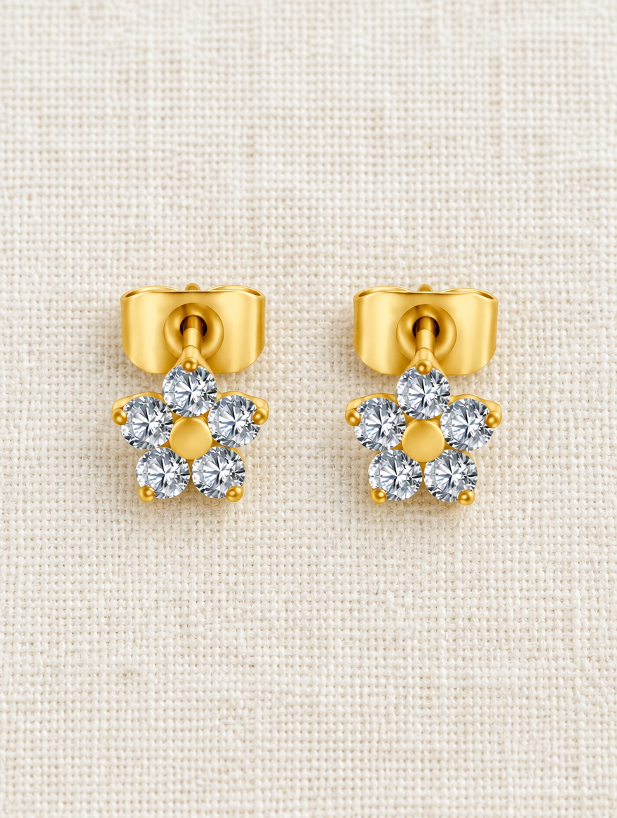Gold titanium CZ flower stud earrings lying flat on a soft styled surface