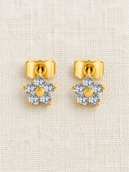 Gold titanium CZ flower stud earrings lying flat on a soft styled surface