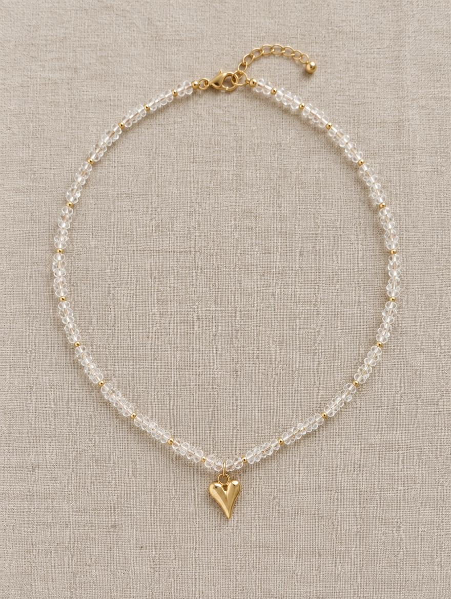 Clear bead choker with gold heart pendant lying on linen