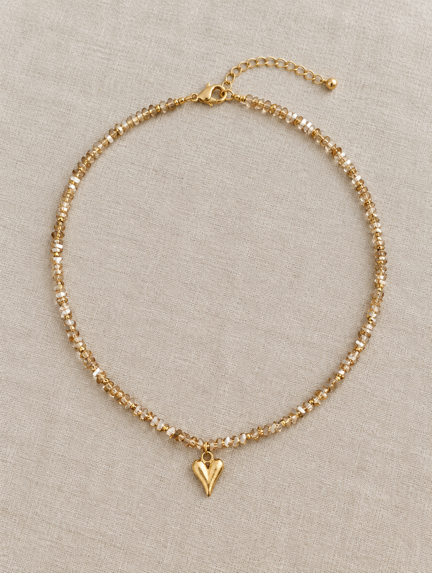 Champagne bead choker with gold heart pendant lying on linen