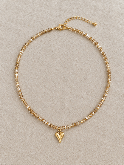 Champagne bead choker with gold heart pendant lying on linen