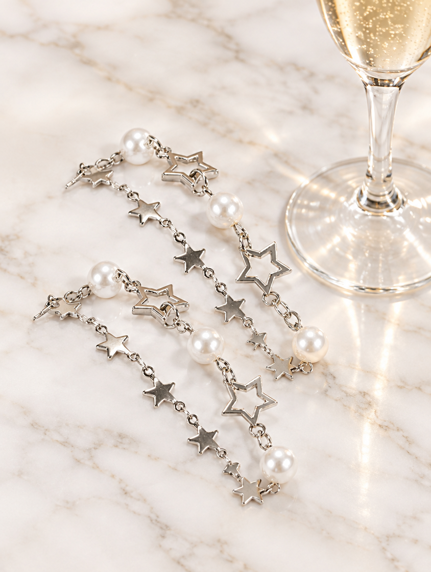 Star chain bracelets with faux pearls beside a champagne flute on marble