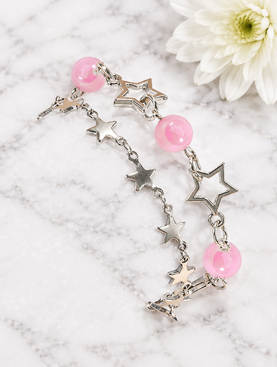 Star chain bracelets with pink beads beside a white flower on marble