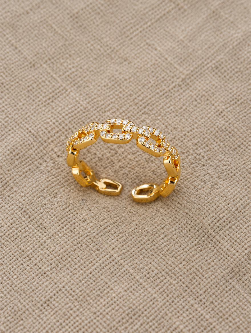 Gold slim chain link zirconia ring resting on a soft textured surface