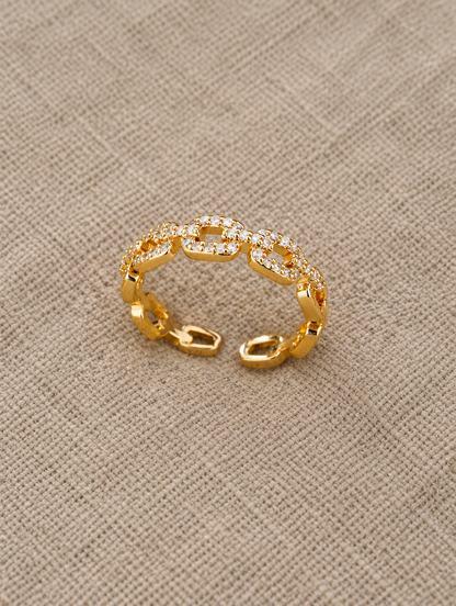 Gold slim chain link zirconia ring resting on a soft textured surface