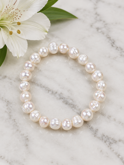 White pearl bracelet beside a white flower on marble
