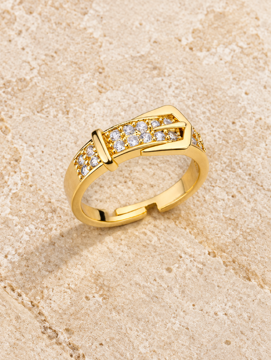Gold belt buckle zirconia ring resting on a soft textured surface