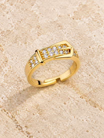 Gold belt buckle zirconia ring resting on a soft textured surface