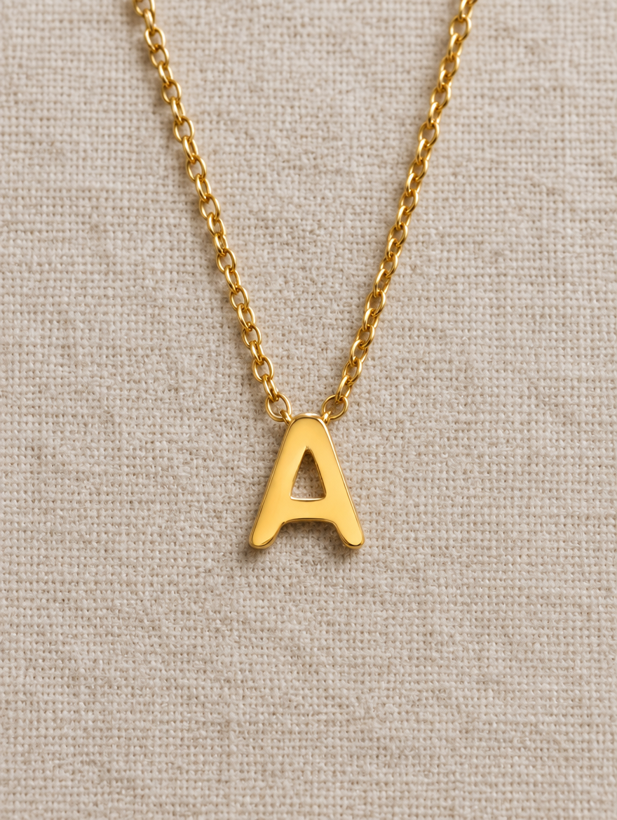 Gold initial letter necklace lying flat on linen