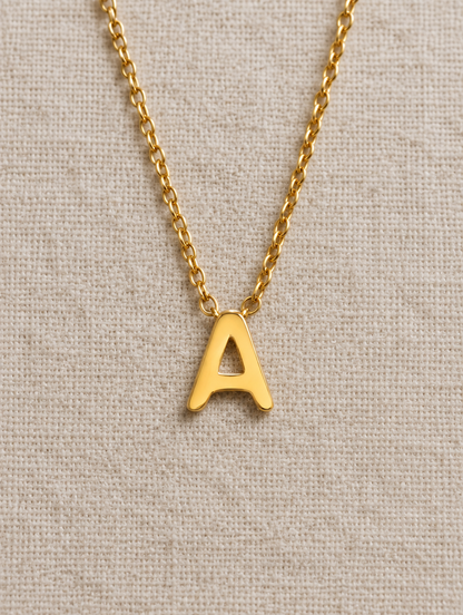 Gold initial letter necklace lying flat on linen
