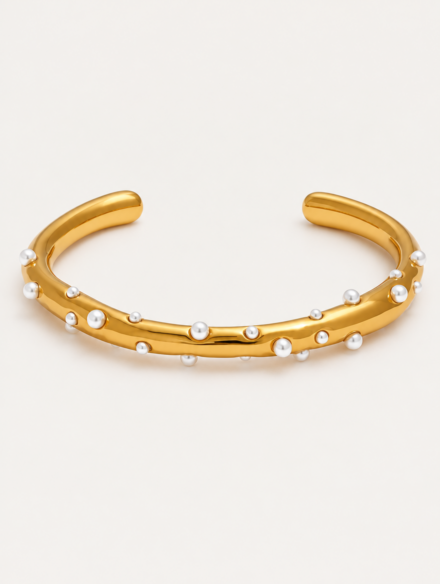 Gold open cuff bracelet with faux pearls on a neutral background