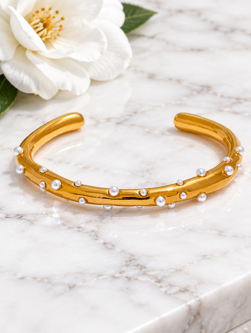 Gold pearl cuff bracelet beside a white flower on marble