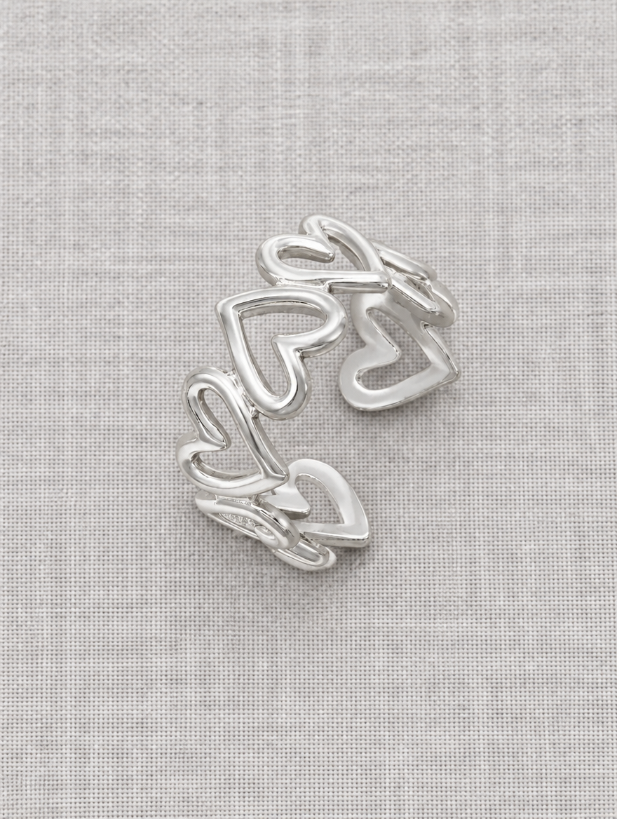 Silver hollow heart outline ring resting on a soft textured surface