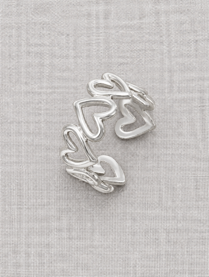 Silver hollow heart outline ring resting on a soft textured surface
