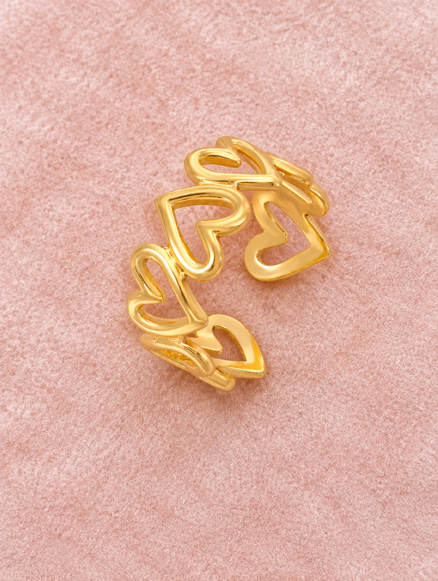 Gold hollow heart outline ring resting on a soft textured surface