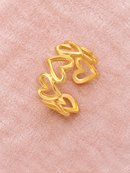 Gold hollow heart outline ring resting on a soft textured surface