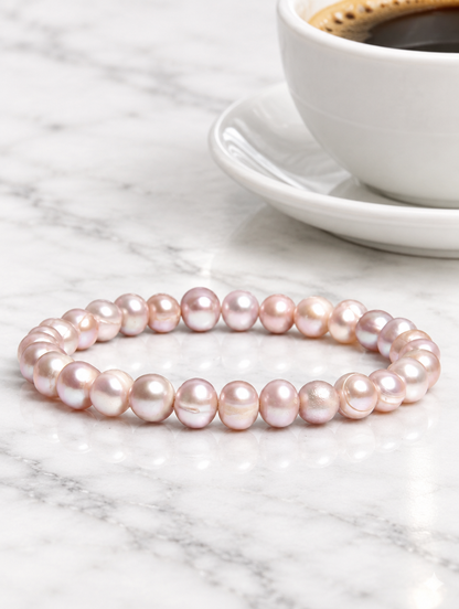 Pink freshwater pearl stretch bracelet beside a pink rose on marble