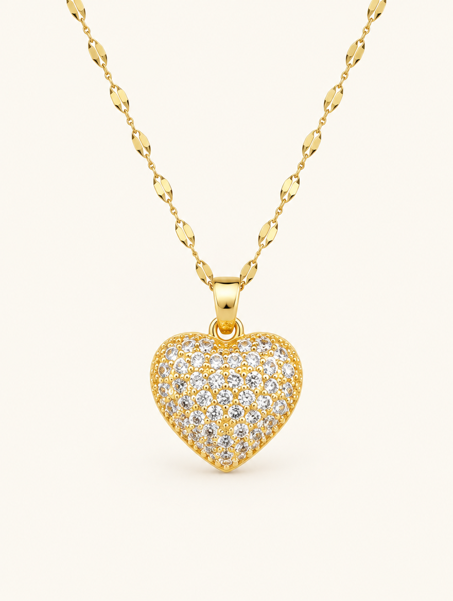Gold necklace with a heart covered in tiny clear crystals on a neutral background