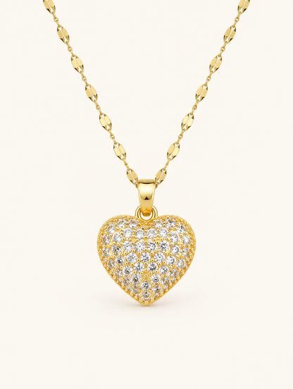 Gold necklace with a heart covered in tiny clear crystals on a neutral background