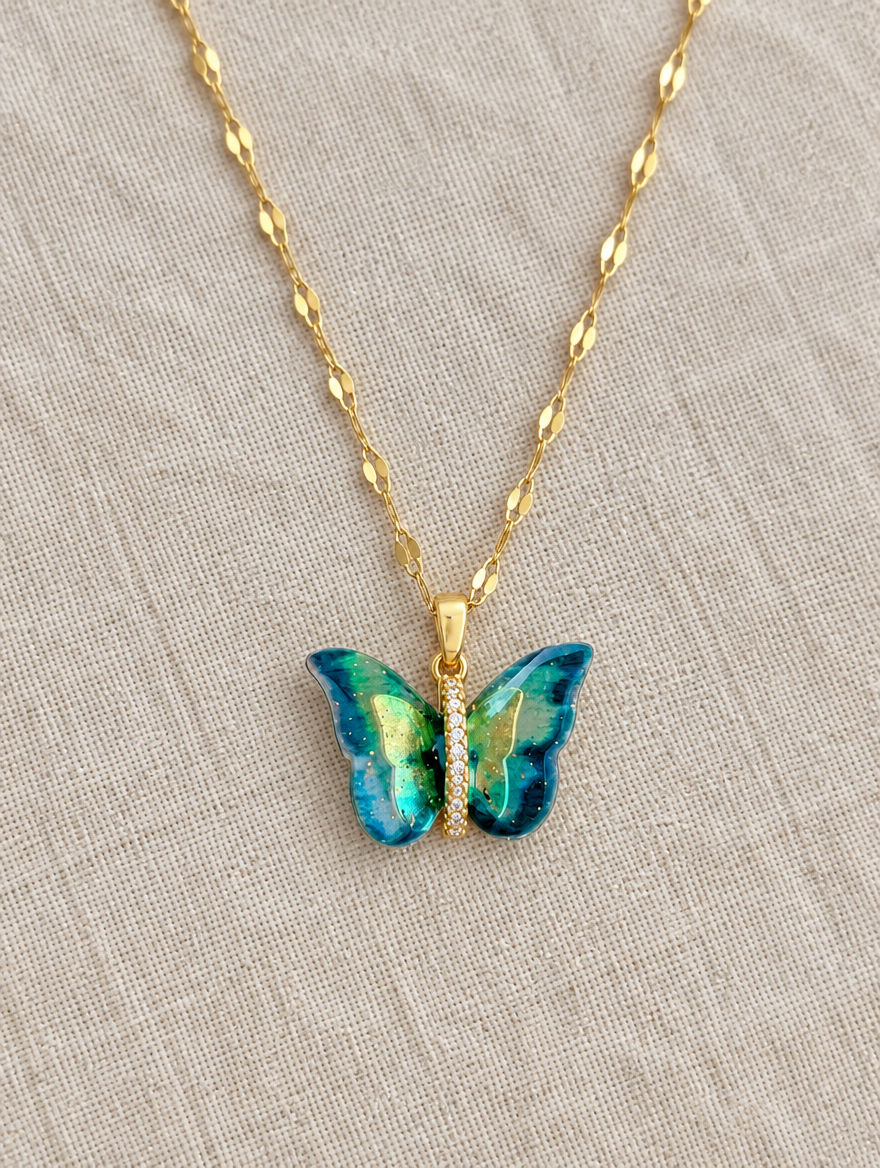 Gold enamel butterfly pendant necklace lying flat on linen