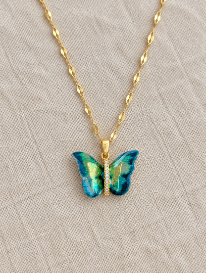Gold enamel butterfly pendant necklace lying flat on linen