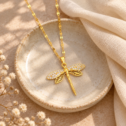 Gold dragonfly pendant necklace on a ceramic dish beside a folded cream scarf