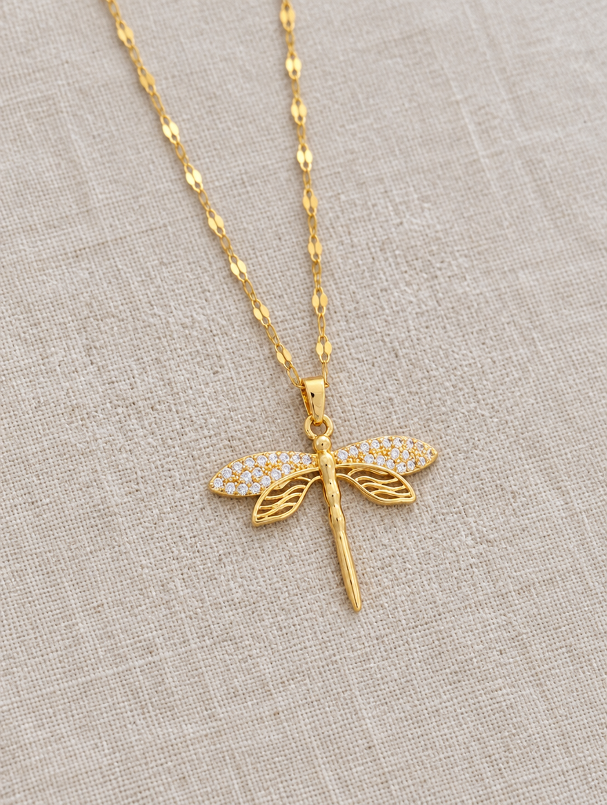 Gold dragonfly pendant necklace lying flat on linen