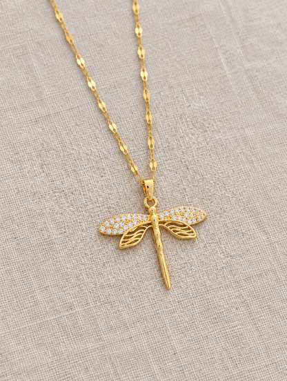 Gold dragonfly pendant necklace lying flat on linen