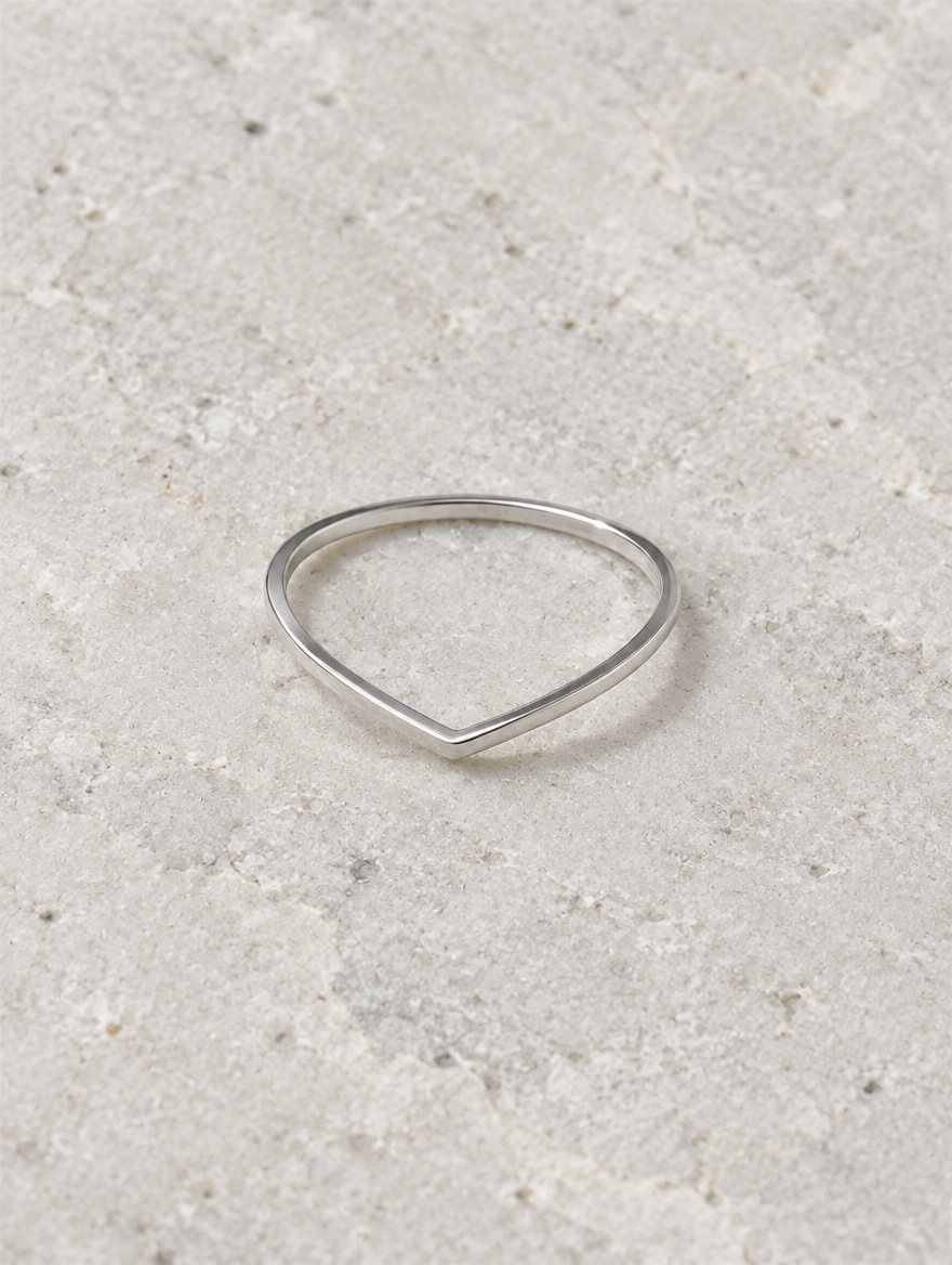 Silver slim chevron band ring resting on a soft textured surface