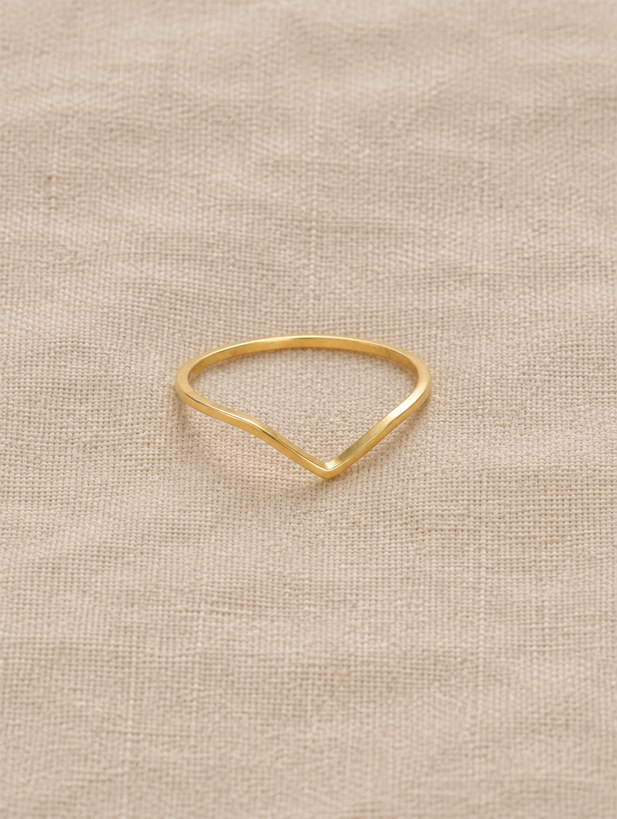 Gold slim chevron band ring resting on a soft textured surface