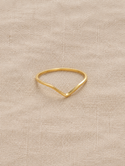 Gold slim chevron band ring resting on a soft textured surface